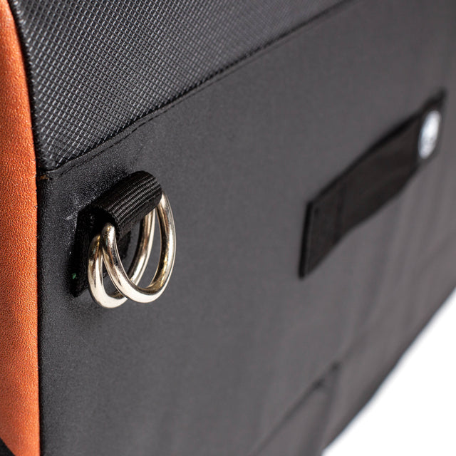 Close-up of the Bells of Steel Soft Glute Bench in black and orange, featuring metal D-rings attached with black fabric on the side and a small rectangular Velcro strap nearby.