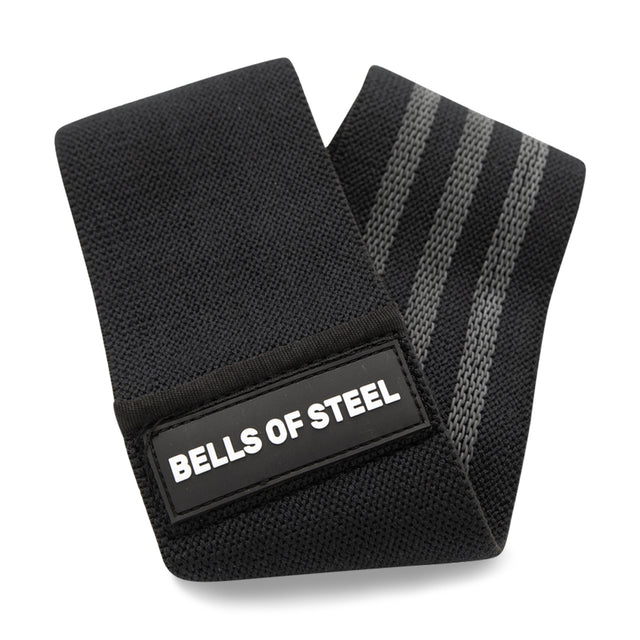 The Bells of Steel Glute Loop is a black fabric resistance band with gray stripes and a rectangular "BELLS OF STEEL" label, ideal for enhancing your next glute workout.