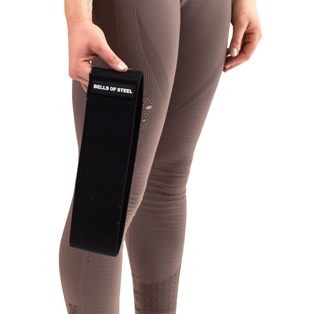 Wearing taupe leggings, a person holds the Bells of Steel Glute Loop resistance band against a white background—ideal for any booty workout.