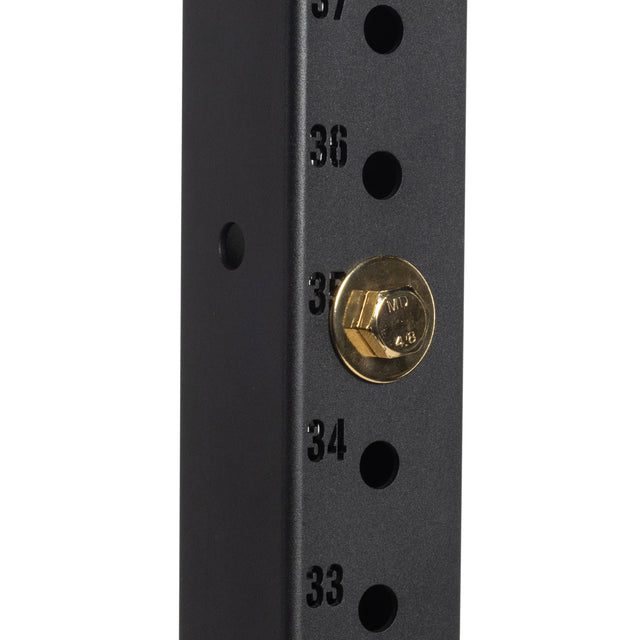 Close-up of a black metal rack with numbered holes (33–37), featuring a Bells of Steel Gold / Black Titanized Bolt for Hydra securely inserted into hole 35.