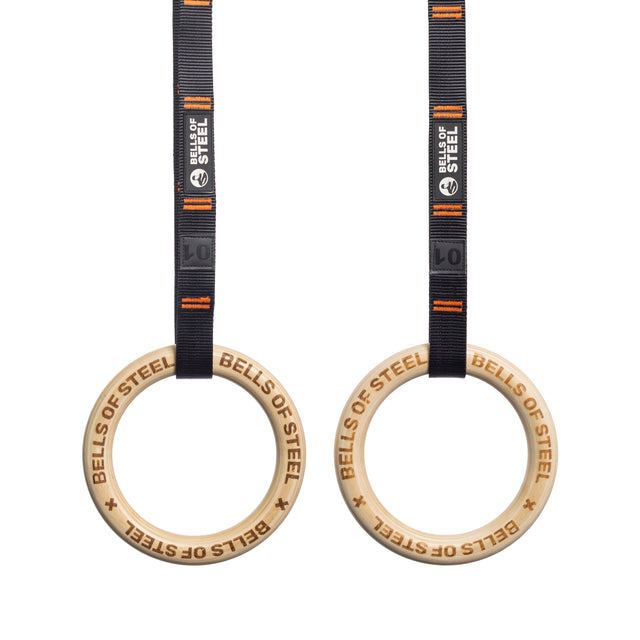 Two Gymnastics Rings from "Bells of Steel" hang on black straps with orange accents. These portable tools are perfect for bodyweight and strength training, featuring the "Bells of Steel" branding.