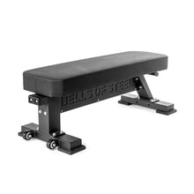The Bells of Steel Hero Heavy-Duty Weight Bench is a black flat bench with sturdy metal legs, “BELLS OF STEEL” cut out on the side, a 1,000lb max capacity, and wheels at one end for easy mobility.
