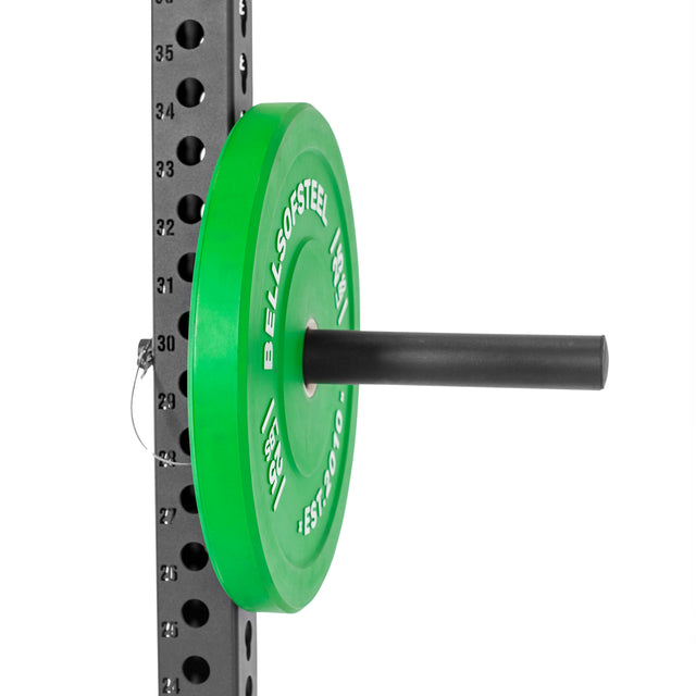 A "BELLS OF STEEL" Olympic weight plate in green is stored on the Utility Horn Rack Attachment, featuring black powder coating and numbered holes for adjustable height.