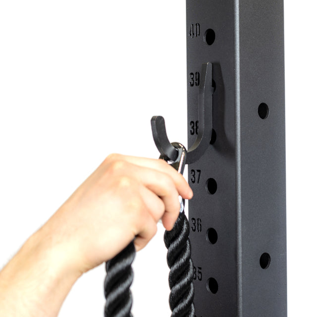 A hand secures a black cable attachment with a metal clip onto the Bells of Steel Utility Hook on a tall, numbered gym rack, with numbers 35 to 40 visible for organized storage.