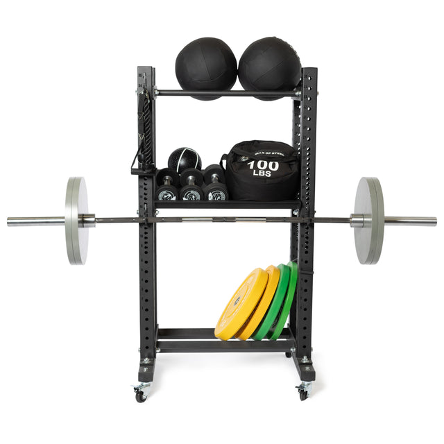 The Bells of Steel Utility Hook keeps medicine balls, kettlebells, a 100 lb sandbag, cable attachments, a barbell with weights, and yellow and green weight plates organized neatly on the rack.