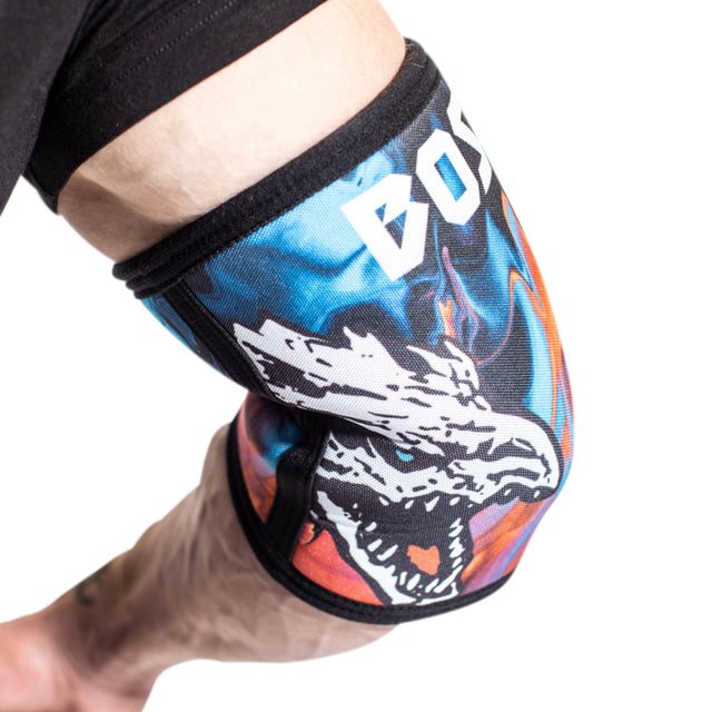 A close-up of an arm wearing Bells of Steel Elbow Sleeves with a colorful design, bold text, and a white wolf head graphic, set against a white background.