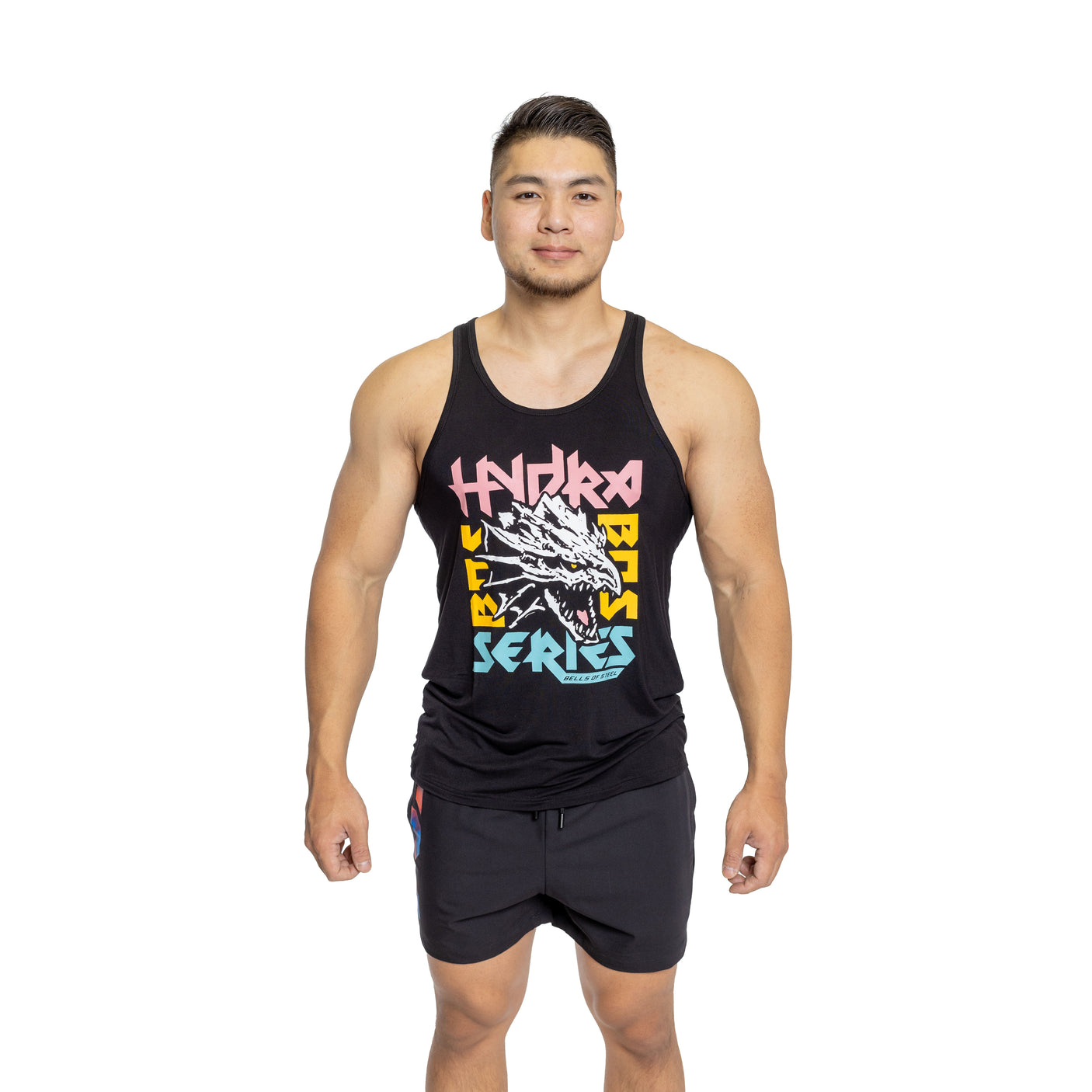A man stands smiling against a white background, wearing Bells of Steel Bamboo Tank Tops featuring colorful graphic text and a dragon design, paired with black shorts, with his arms relaxed at his sides.