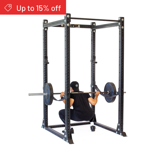 A person in black workout clothes performs a squat with a barbell inside the Bells of Steel Hydra Flat Foot Power Rack Builder (3" x 3", ⅝" Holes). A red banner reads "Up to 15% off." Perfect for your home gym setup.