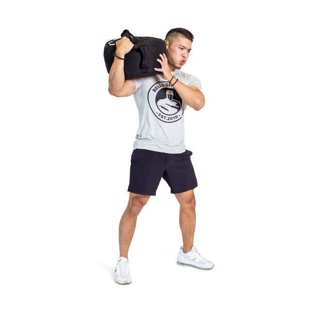 A man in athletic wear lifts a Bells of Steel Fitness Sandbag Set onto his shoulder against a white background, demonstrating effective sandbag workouts.