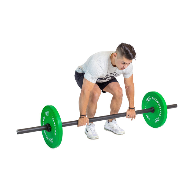 A man in a light gray shirt, black shorts, and white sneakers prepares to deadlift the Bells of Steel Axle Bar with large green weights—ideal for grip strength and strongman training—against a white background.