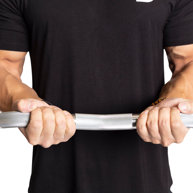 A person in a black t-shirt holds a bent Easy Curl barbell from Bells of Steel, showcasing strength and grip. The white background highlights the focus on Fixed Barbells and the person’s muscular arms, ideal for any home gym enthusiast.