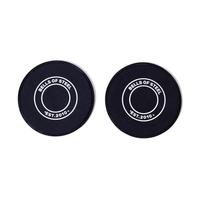 Two Bells of Steel Core Sliders, black with white rings and “BELLS OF STEEL EST. 2010” in the center, are shown side by side on a white background—ideal for total body workouts like sliding hamstring curls.