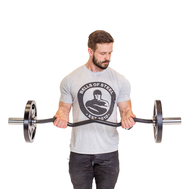 A man in a gray Bells of Steel t-shirt and black pants holds the Bells of Steel EZ Curl Bar (45") at waist height, focusing on arm development, against a plain white background.