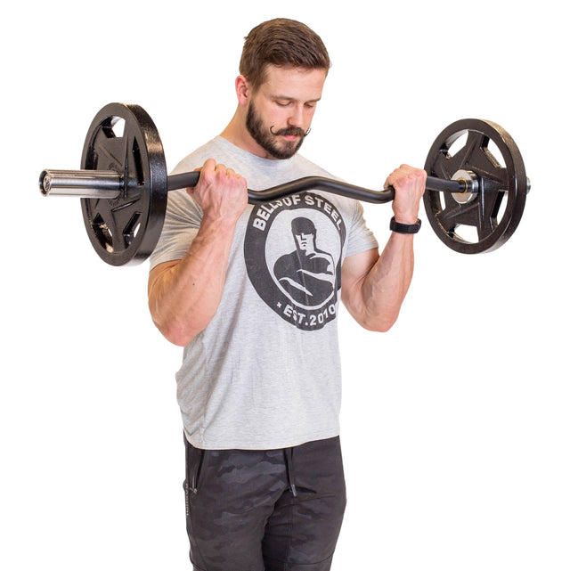 A bearded man in a gray t-shirt and black pants performs bicep curls with the Bells of Steel EZ Curl Bar (45"), looking down at the weights against a white background.