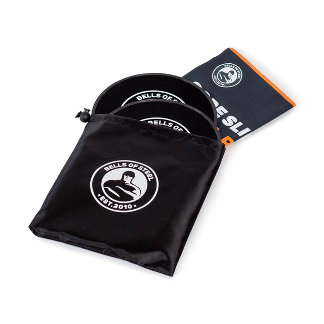 A pair of black Bells of Steel Core Sliders, partially in a branded drawstring pouch, are shown next to an orange and black total body workout instruction booklet.