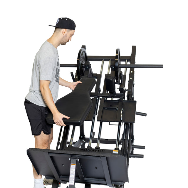 A man in athletic wear adjusts the bench of a Bells of Steel 2-in-1 Iso Leg Press & Hack Squat Machine (The Juggernaut) with weight plates, isolated on a white background.
