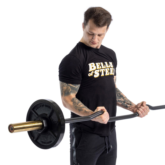 Wearing a Bells of Steel shirt, a person performs bicep curls with the Rackable EZ Curl Bar, focusing on optimal arm development.
