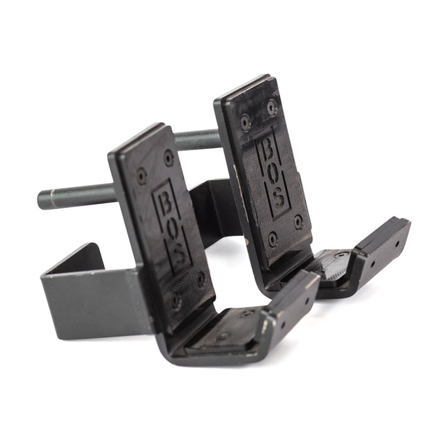 Two black metal wall-mounted Standard J-Cups by Bells of Steel, with adjustable arms and "BOS" embossed on the front, designed for holding items like bikes or tools. The angled hooks have UHMW-protected arms for extra durability.