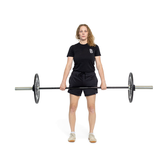 A woman in a black t-shirt and shorts stands holding the Bells of Steel Juno Bar - Women's Utility Bar with weights, arms extended down, against a white background.