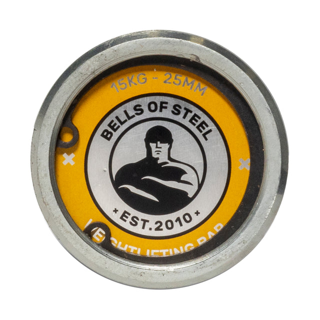 Close-up of a round metal plate on a yellow background showing the "Bells of Steel" logo, "EST. 2010," and "15KG - 25MM"—designed for the Juno Bar - Women’s Utility Bar by Bells of Steel, ideal for small hands.