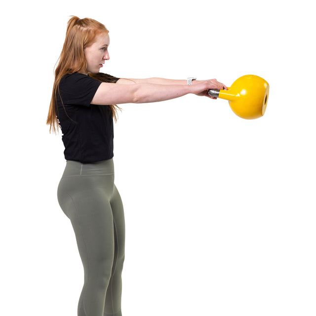 A woman with long red hair, in a black shirt and olive leggings, swings a yellow Bells of Steel Competition Kettlebell against a white background.
