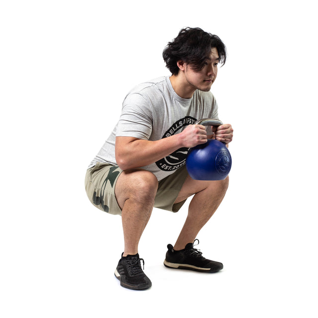 A man in a light gray t-shirt and camo shorts squats while holding a blue Bells of Steel Competition Kettlebell with both hands, against a white background.