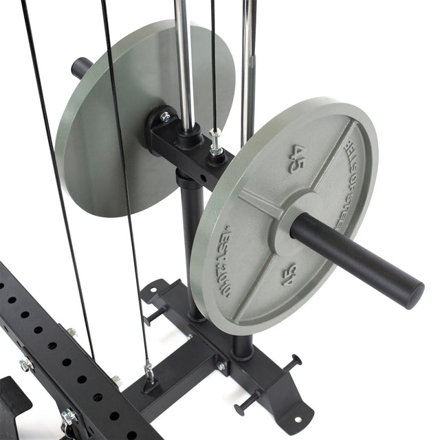 Close-up of Bells of Steel gym equipment showing two large gray 45-pound Olympic weight plates on a black rack. The setup includes a Hydra & Manticore Lat Pulldown & Low Row Rack Attachment with cables and metal rods, suggesting a weight lifting or resistance exercise machine.