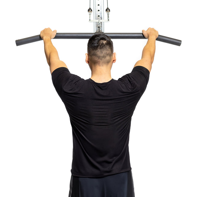 A man seen from behind, in a black shirt, holds the Bells of Steel Fat Bar - Lat Pulldown Bar cable attachment, preparing for a lat pulldown exercise to boost grip strength against a white background.