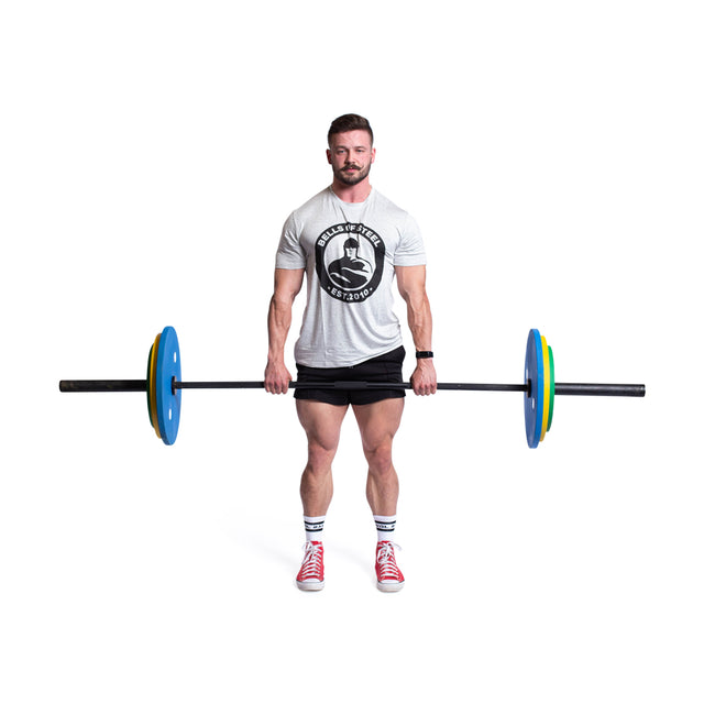 Wearing a gray T-shirt, black shorts, and red sneakers, a person stands on a white background lifting the Bells of Steel's Calibrated Powerlifting Plates - LB Sets to showcase their strength.