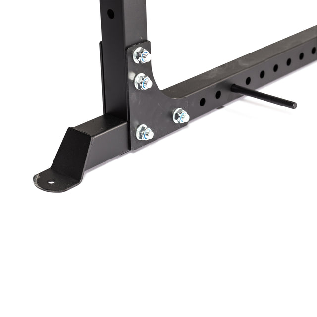 Close-up of the Bells of Steel Light Commercial Power Rack (2.3" x 2.3", ⅝" holes), featuring a black metal frame with bolts, a bracketed foot, and a horizontal bar with holes and an inserted metal pin for barbell safety during home workouts.