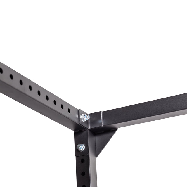 Close-up of a Bells of Steel Light Commercial Power Rack (2.3" x 2.3", ⅝" HOLES) corner joint, showing three black metal beams bolted together. One beam features evenly spaced holes. Plain white background.