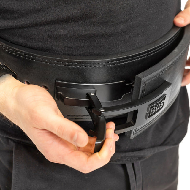 A person fastens a thick black Bells of Steel Lever Belt with a metal buckle over black shirt and pants, preparing for powerlifting.