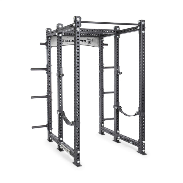 The Manticore Six Post Power Rack by Bells of Steel is a sleek black unit with 1" holes for adjustable attachments, a pull-up bar, safety straps, logo branding, and side weight plate holders—it's an open ecosystem for versatile strength training exercises.