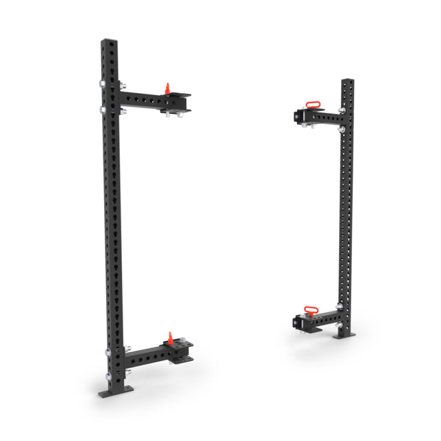 Two black Bells of Steel Manticore Folding Half Rack uprights (3" x 3", 1" holes) with red-handled adjustable brackets stand separately—modular, prebuilt home gym equipment for versatile rack setups.