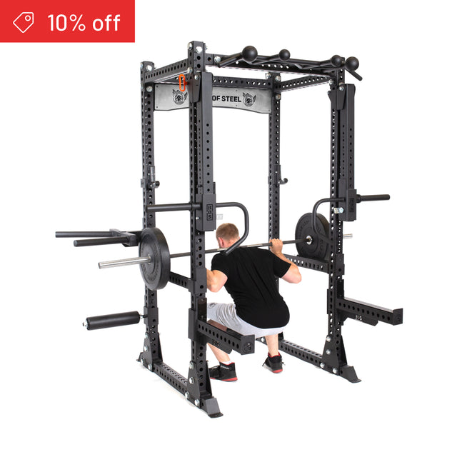 A man squats with a barbell in the Bells of Steel Manticore Flat Foot Power Rack Builder (3" x 3", 1" Holes). A red "10% off" sale tag appears in the top left—ideal for enhancing your home gym.