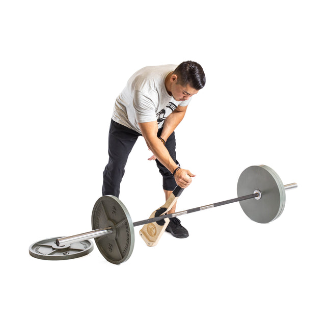 A man in a gray T-shirt and black pants uses the Bells of Steel Meat Hook Deadlift Jack to grip and lift a loaded barbell from the floor against a white background.