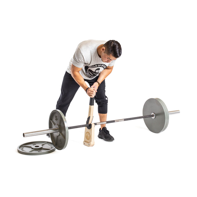 A man uses the Bells of Steel Meat Hook Deadlift Jack to lift a barbell, making it easy to change weight plates. One plate rests on the ground nearby. The plain white background highlights this portable weightlifting tool.