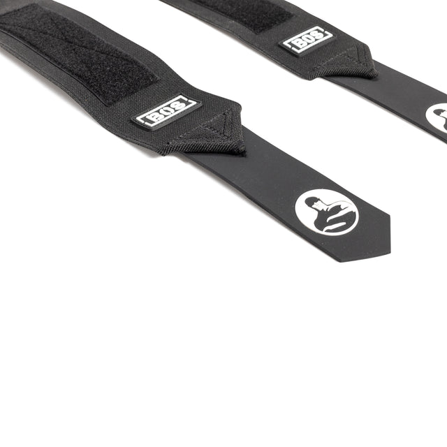 Two black Mighty Wrist Wraps by Bells of Steel with Velcro sections, reinforced ends, and a white helmeted logo. "Bells of Steel" appears on the tags. Essential for powerlifting, they're displayed on a white background.