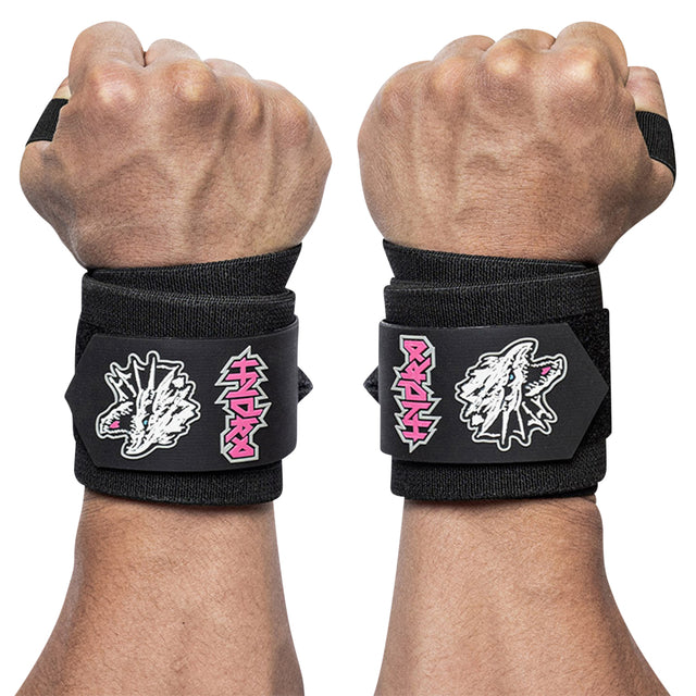 Two hands wear Bells of Steel Mighty Wrist Wraps—black with white dragon head graphics and pink text. These powerlifting essentials offer wrist support, secured by wide black straps and velcro closures.