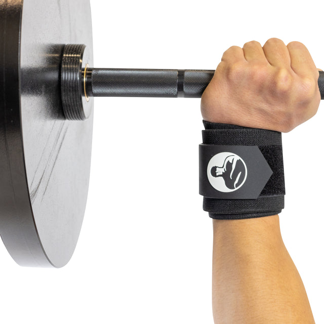 A close-up of a hand gripping a barbell with weight plates, wearing Bells of Steel Mighty Wrist Wraps—black wraps featuring a white flexed bicep logo for essential powerlifting support.