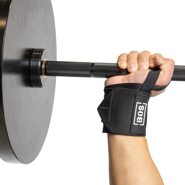 A person’s hand grips a barbell with weight plates, wearing black Mighty Wrist Wraps by Bells of Steel—a powerlifting essential—against a plain white background.