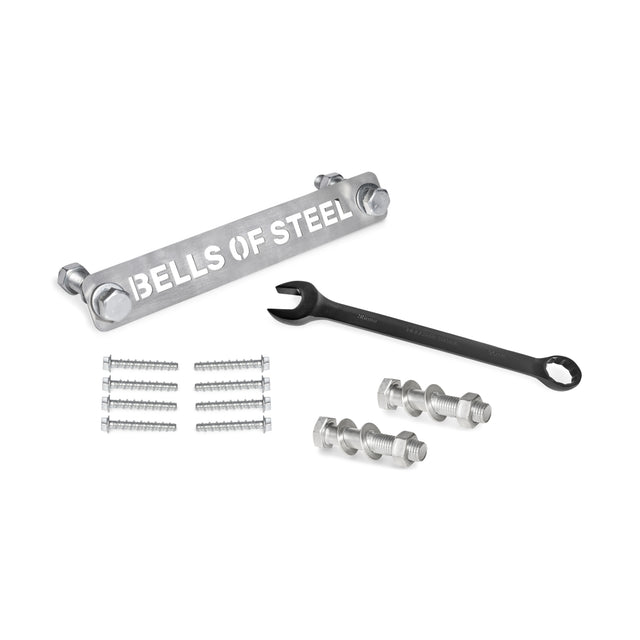 A metal bar labeled with "Bells of Steel" sits beside a combination wrench, with silver screws and nuts neatly organized as part of the Manticore Hardware kit.