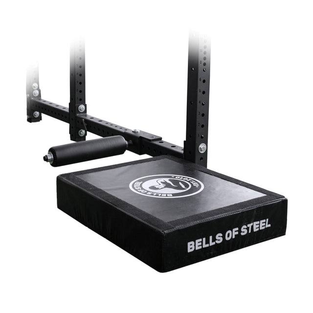 The Bells of Steel Hydra Nordic Curl Package is a padded platform attachment for metal gym racks, featuring a logo on the pad and a cylindrical roller bar, ideal for exercises like split squats and Nordic hamstring curls.
