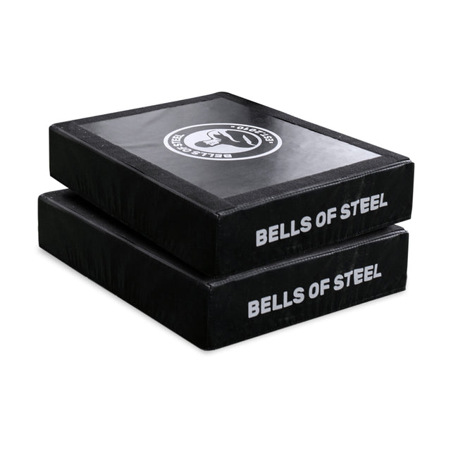 The Bells of Steel Hydra Nordic Curl Package includes two black foam pads with white "BELLS OF STEEL" branding, stacked together—perfect for Nordic hamstring curls or adding a split squat attachment to your gym setup.