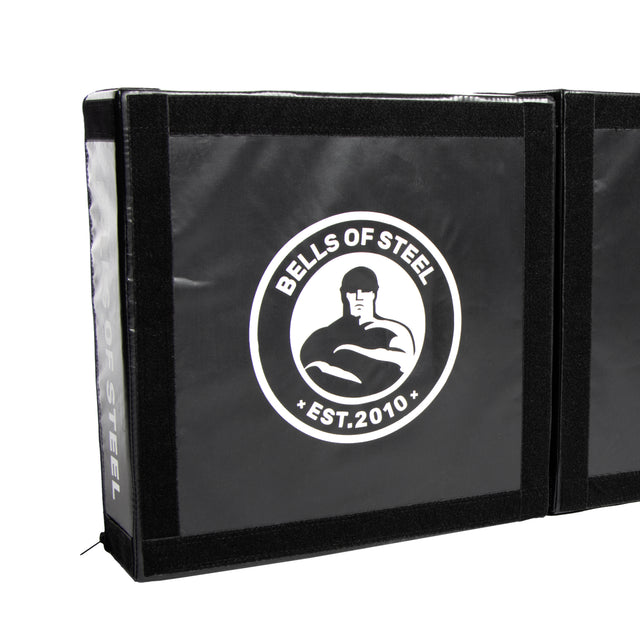 The Bells of Steel Deadlift Platform Drop Pad Pair is a black crash mat featuring the "Bells of Steel Est. 2010" logo and a white muscular figure, designed to absorb impact and reduce noise during heavy lifts.