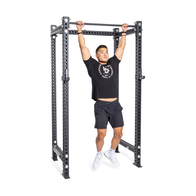 A confident man in a black shirt and shorts performs a pull-up on the robust Bells of Steel Straight Pull Up Bar, ideal for strength training, set against a plain white background.