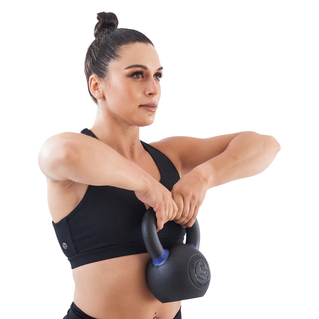 A woman with a strong grip lifts the Bells of Steel Powder Coated Kettlebell to chest height in an upright row against a plain white background.