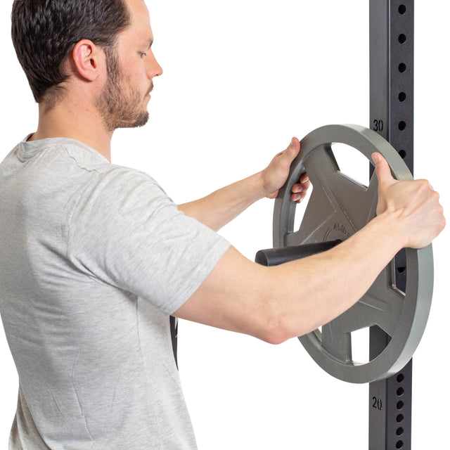 A man in a gray T-shirt places a large Olympic weight plate onto Bells of Steel Pin Plate Pegs, convenient power rack accessories for organized storage.
