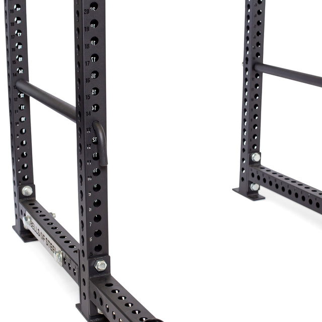 Close-up of Bells of Steel Pin Pipe Safeties inserted into a black steel power rack with numbered holes; the floor and rack base are also visible.