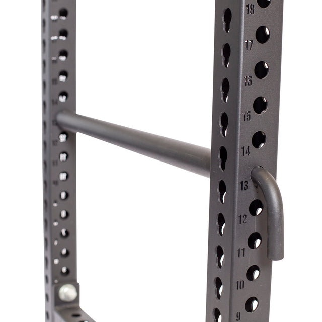 Close-up of a Bells of Steel black metal power rack featuring Pin Pipe Safeties for protection, and numbered holes with printed guides for easy height adjustment. A horizontal bar connects the vertical posts.